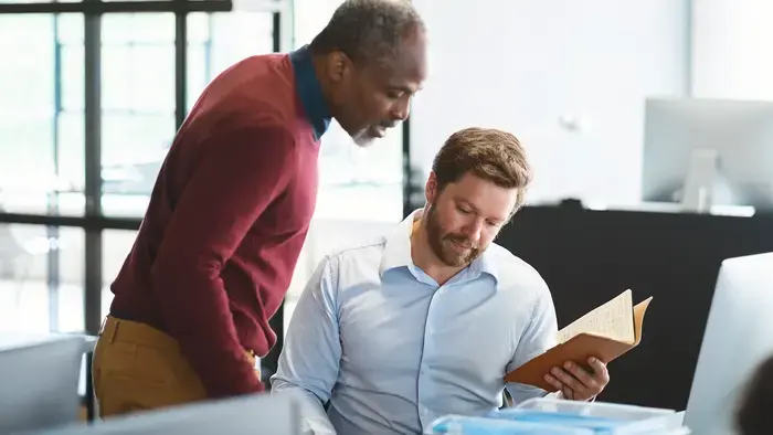 Two men in an office review papers, notes
