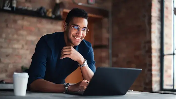 Smiling man, working on a laptop; he is a full-time employee.