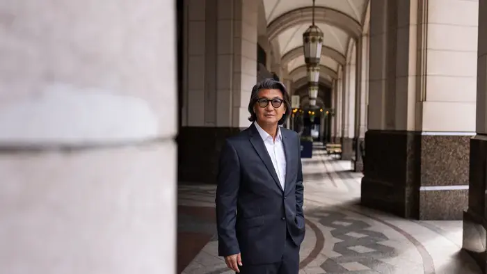 A person wearing glasses and a suit stands on a pathway.