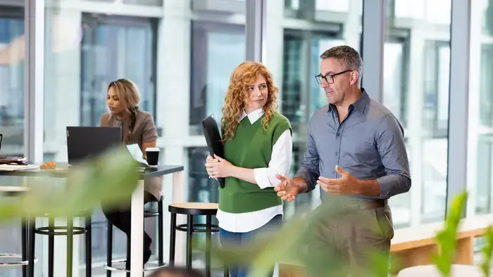 Two coworkers converse in a modern office.