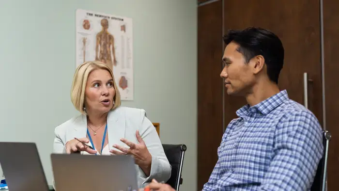 A woman and man converse in a doctor's office with laptops.