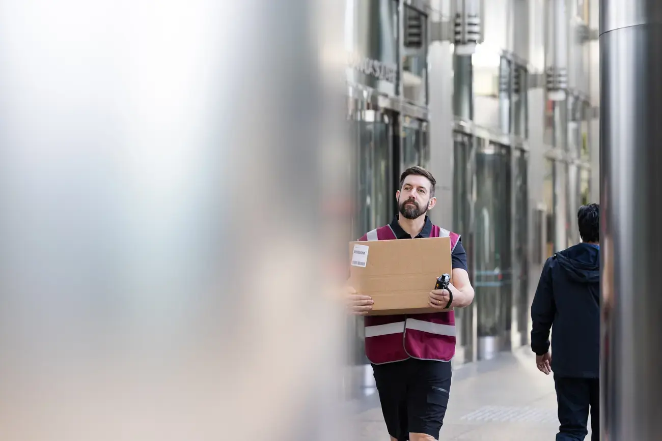 A man carries a box through a building hallway.