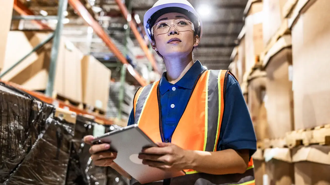 A person in a warehouse, holding a tablet, looking up.