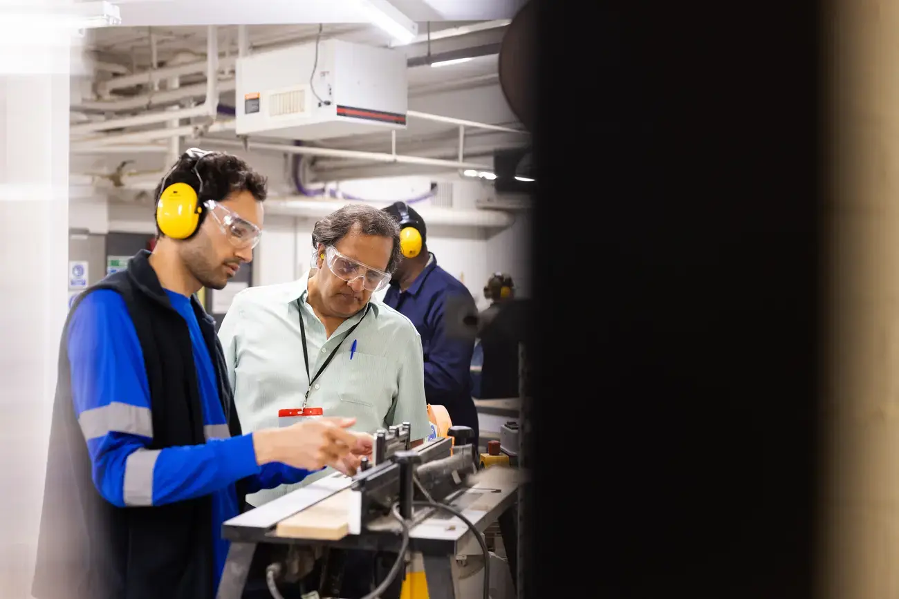 Workers wearing hearing protection operate machinery.