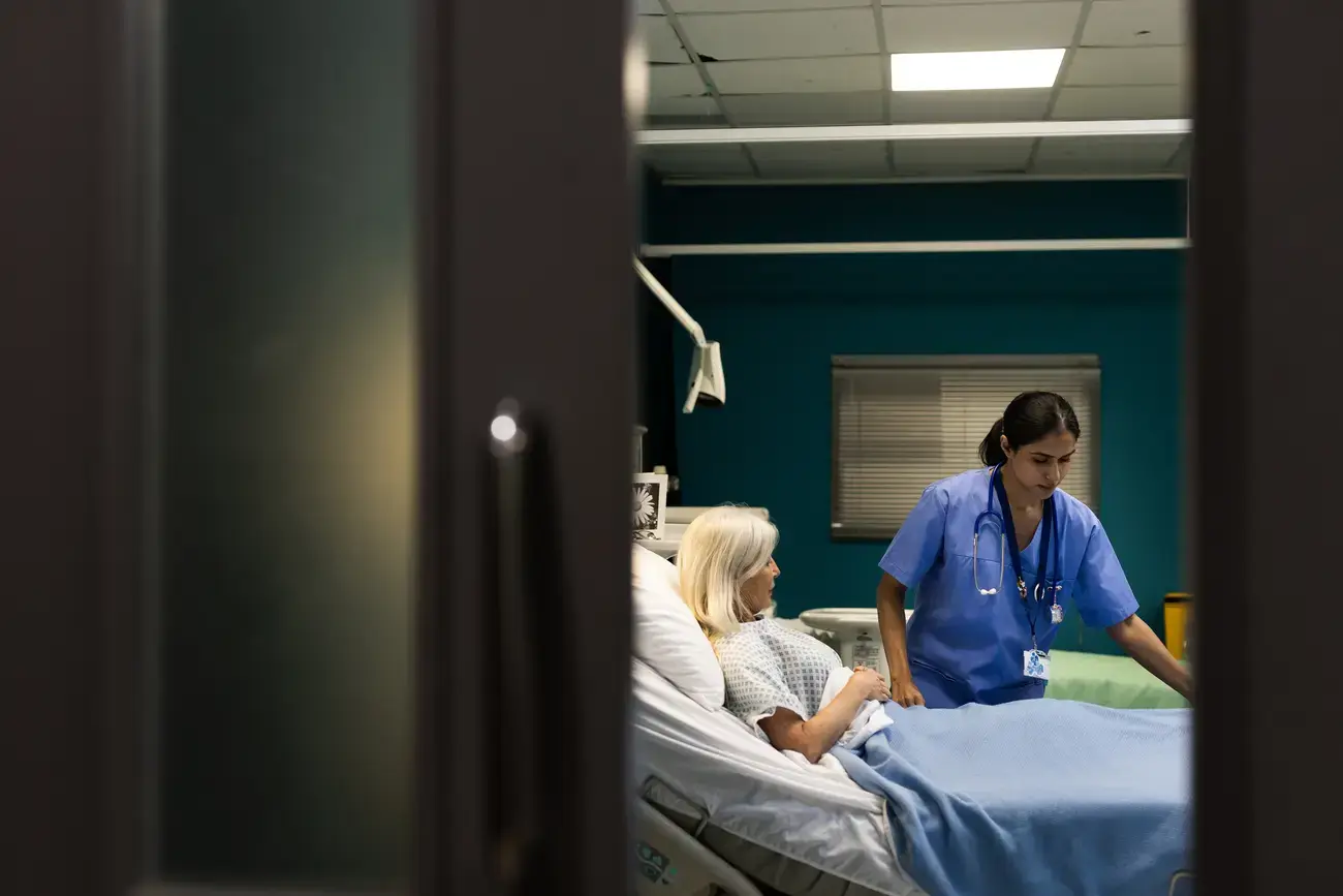 Nurse assisting elderly patient in hospital bed.