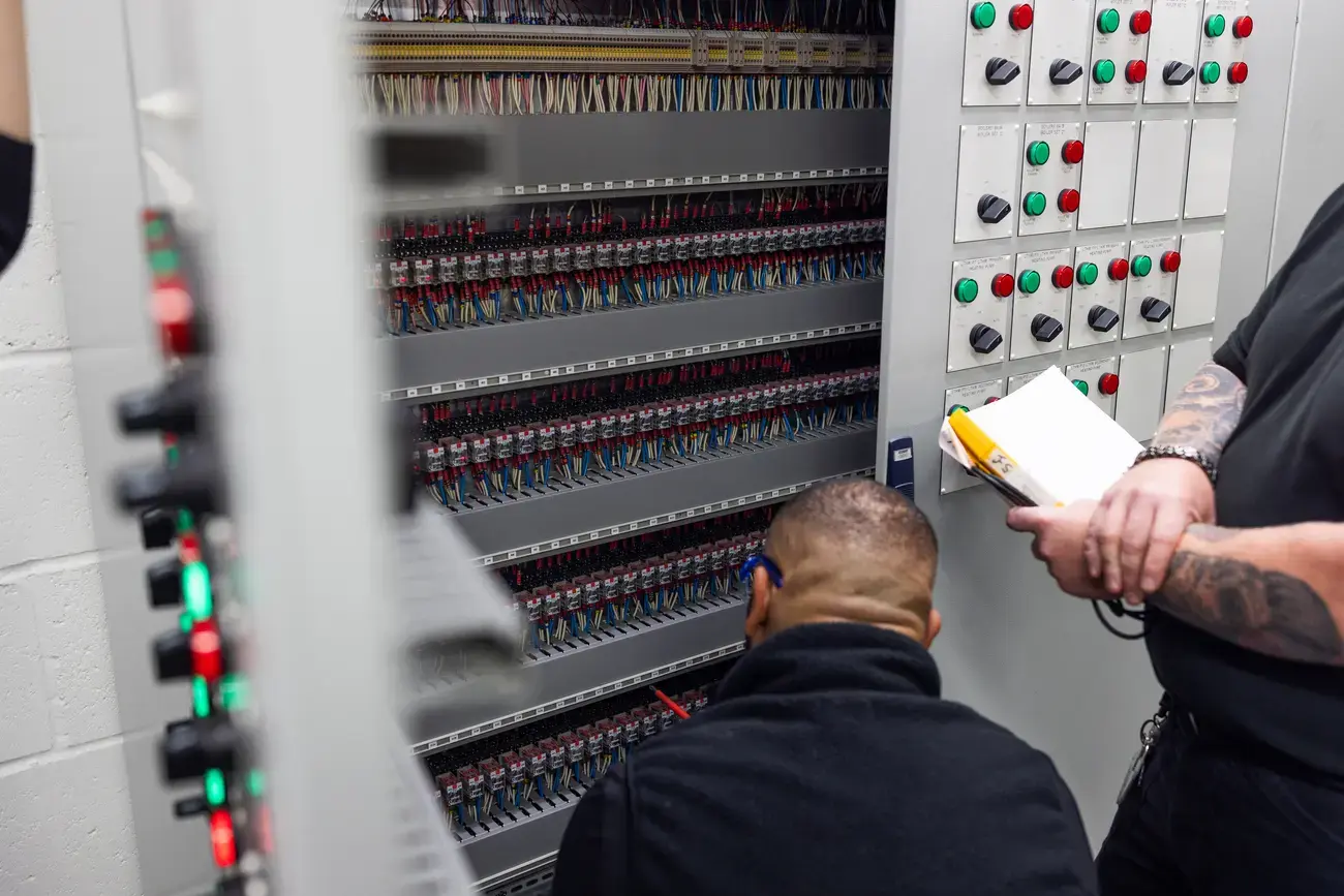 Two technicians inspect electrical control panels.