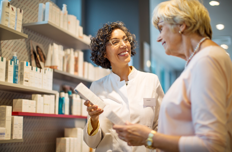 A pharmacist and a customer are standing in a pharmacy looking at a box of medication.
