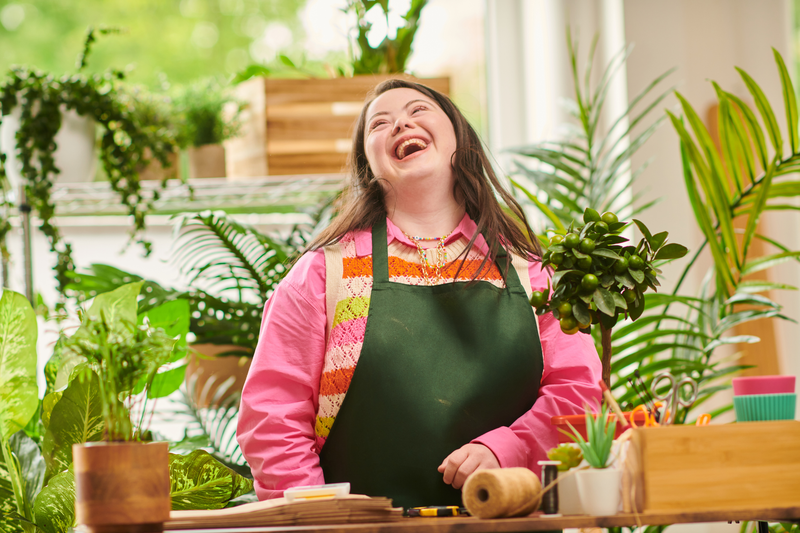 A woman wearing a pink shirt and green apron laughs happily while working.