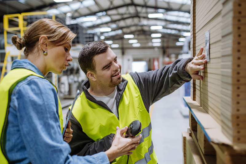 A man and woman in a warehouse are looking at a product label.