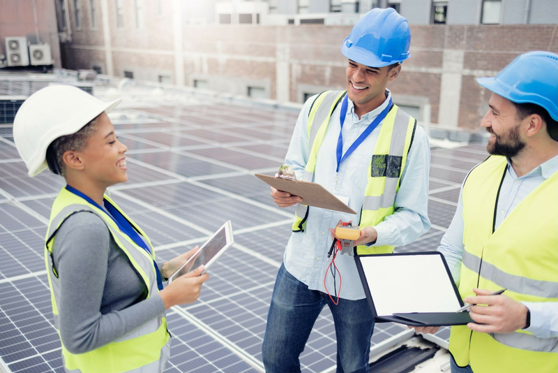 Three people wearing hard hats are working together to install solar panels on a rooftop.